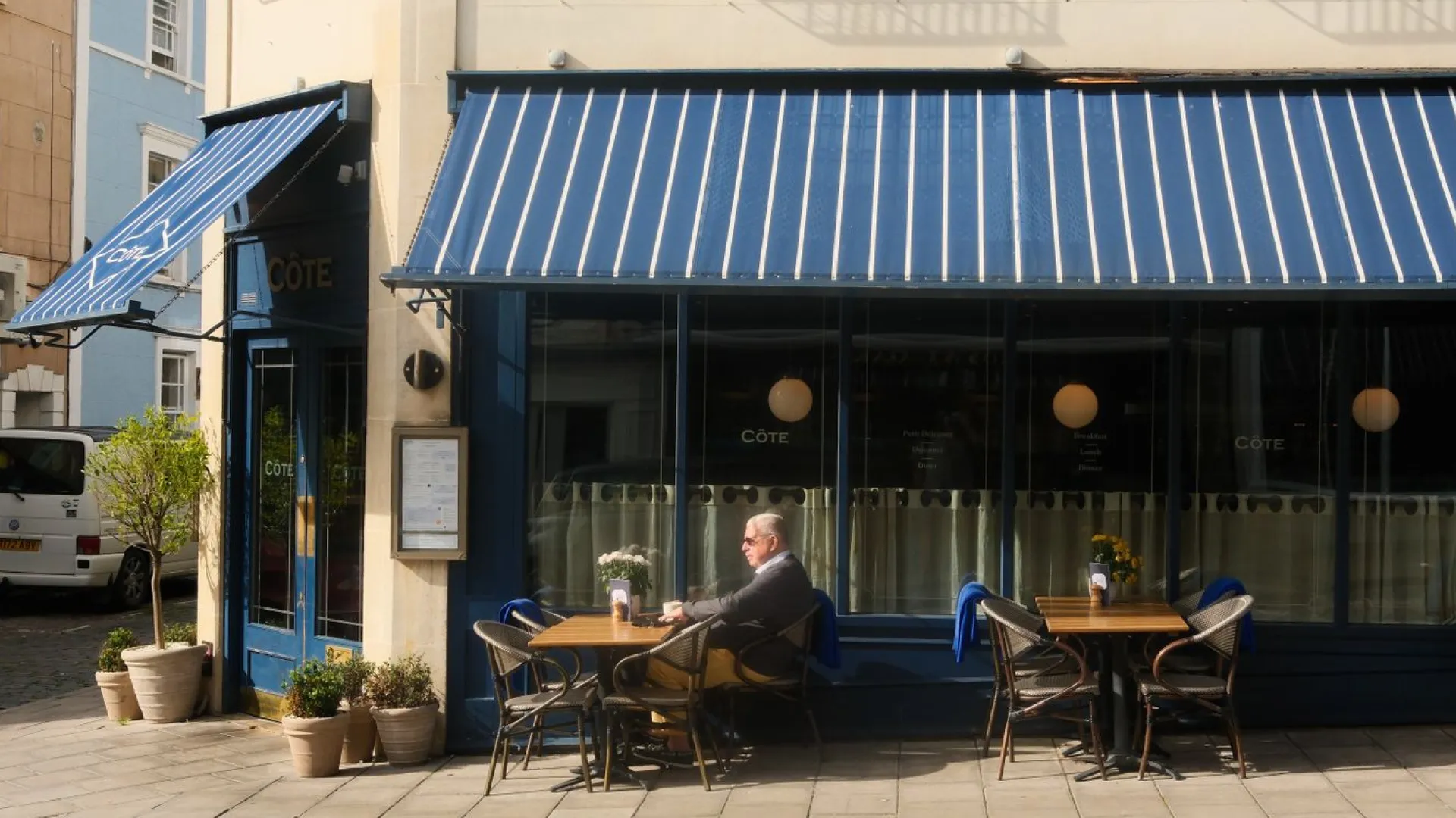 Man sitting outside restaurant with blue-white awning on top of him in Eatontown, NJ